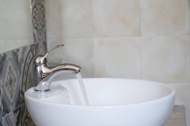 Parlatılmış bir musluktan parlak beyaz bir lavaboya temiz su akıntıları. Kaynak israfı ve çevresel sorumsuzluk. Yüksek kalite fotoğraf