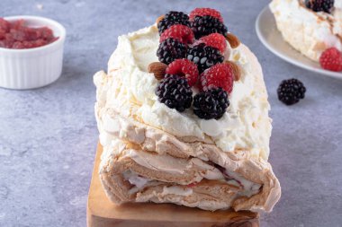 Krema ve ahududu ve böğürtlen ile süslenmiş ahşap bir tahtanın üzerinde sunulan kremalı bir tatlı. Tatil kutlamaları ya da özel günler için mükemmel. Yüksek kalite fotoğraf