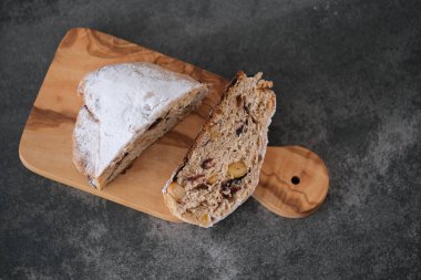 Ahşap bir tahtanın üzerinde duran bir dilim stollen ekmeğin dokusunu ve malzemelerini sergiliyor. Tatil sezonunu işaret eden dekorasyonlarla oluşturulmuş şenlikli bir atmosfer. Üst Manzara. Yüksek kalite fotoğraf