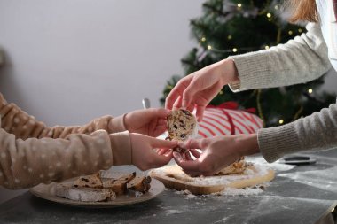 Noel süslemeleriyle süslenmiş sıcak aydınlatılmış bir mutfakta iki kişi taze pişmiş kurabiyeleri değiş tokuş ediyor. Un tezgahın üstüne yayılıyor ve neşeli bir atmosfer yaratıyor. Yüksek kalite fotoğraf