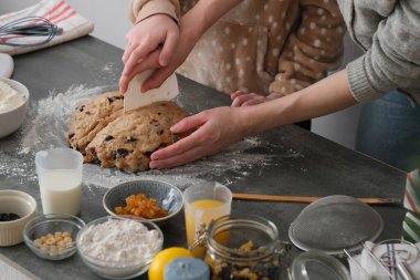 İki birey, zengin, meyve dolu bir hamuru gri bir tezgahta yoğurmak için birlikte çalışıyorlar. Un, meyve ve süt gibi bileşenler onları çevreleyerek sıcak ve işbirlikçi bir atmosfer yaratır. Yüksek kalite fotoğraf