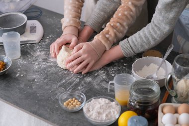 Bir çocuk hamuru yoğurmaya odaklanırken bir yetişkin sıcak bir mutfakta asistanlık yapıyor. Tezgah mutfak aletleri ve pişirmek için malzemelerle dolu. Yüksek kalite fotoğraf
