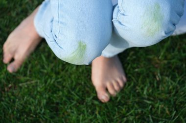 Close up of dirty grass stains on blue jeans person relaxes on soft grass, barefoot on a sunny day outdoors, enjoying nature. top view. Concept of daily stains on clothes. High quality photo