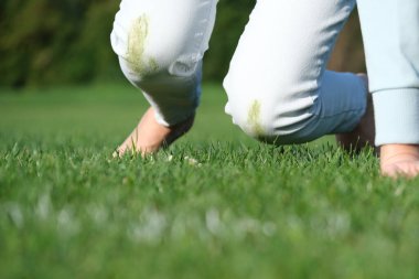 A person falling on green grass wearing white jeans, low angle from below. Outdoor accident, grass stains on clothes, summer lifestyle. The concept of daily stains on clothes. High quality photo