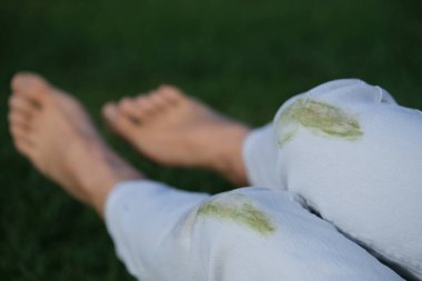 A player in white jeans kneels on the grass during a break in a game. Green stains visible on the knees of the jeans, showing the playfulness of the outdoor badminton match. Concept of daily stains on clothes. High quality photo