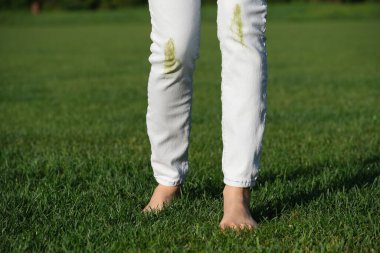 A person falling on green grass and showing a dirty spot on wearing white jeans. Outdoor accident, grass stains on clothes, summer lifestyle. The concept of daily stains on clothes. High quality photo