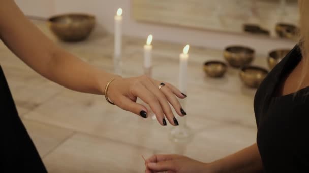 女性的手在女性的手腕上系了一根红线 作为好运与和平的祝福 在藏人碗和点燃蜡烛背景下的宗教仪式 — 图库视频影像