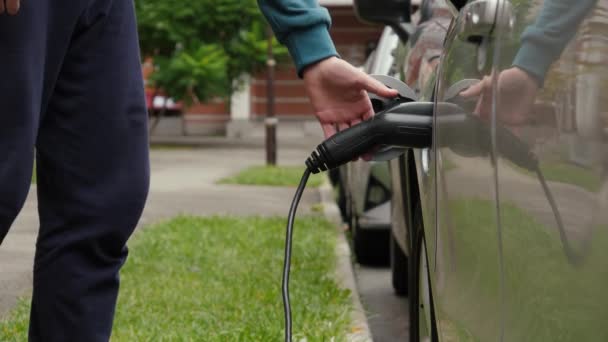 認識できない男は電気自動車に充電ケーブルを切断します 男性の手はEv車への電源コネクタをプラグ解除 — ストック動画