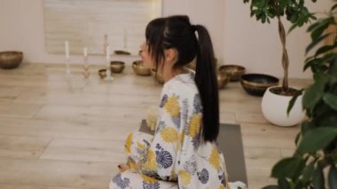 Tibet kâselerinin ve yanan mumların arkasında yoga egzersizi yapan güzel bir kadın.