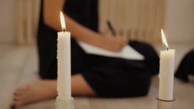 Arka plandaki muma siyahlı genç bir kadının bulanık eli not defterine yazıyor, ödev yapıyor. Yaşam tarzı ve evde çalışma kavramı. Kadın yazar eli, yakın plan.