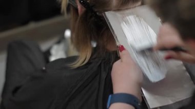 Ustaların eli saç boyası sürerken, saç fırçasıyla kadın saçlarını özel folyo yaprağına sürükler. Kopya alanı. Güzellik salonunda profesyonel bir ustanın ön plana çıkarma süreci. Saçı yakın plan boya.