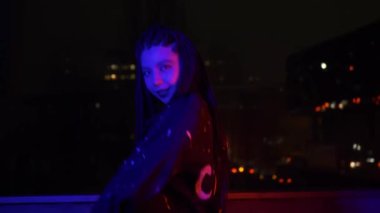 Neon moda Asyalı kadın flört eder ve gece caddesinde yavaşça dans eder. Hipster Vaporwave trendi. Çok renkli kırmızı ışıkta kameraya bakan havalı genç Japon densörü. Şehir tarzı