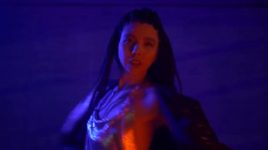 Saçlarını ören, flört eden, geceleri yavaşça dans eden, sığ odaklı Asyalı çekici bir kadın. Güzel seksi kız kameraya bakıyor, kırmızı ve mavi ışık, şehir tarzı.