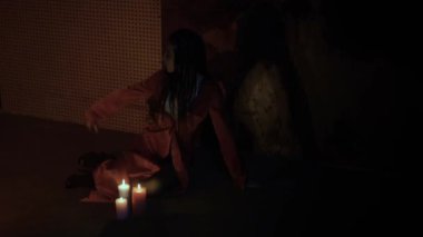 Saçları örgülü seksi Asyalı kadın yavaşça dans ediyor ve karanlık odada mumların yanında kolunu sallıyor.