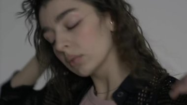 Siyah elbiseli güzel kıvırcık kadın portresi beyaz bir fotoğraf stüdyosunun siklonamasında yavaşça dans ediyor.