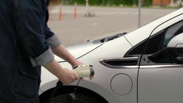 ひげ付きの男は電気自動車に電源コネクターを挿入する デニムジャケットの男は 充電ケーブルを電気自動車に接続し バッテリーを充電します 電気自動車ステーション ゼロエミッション — ストック動画