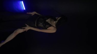 Siyah arka planda dans eden örgülü saçlı Asyalı çekici kadının dikey videosu. Güzel seksi kız kameraya bakıyor, flört ediyor, mavi ışık, şehir tarzı