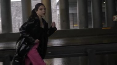 Asyalı kadın kameraya bakıyor ve elinde arabalarla yola doğru koşuyor. Siyah ceketli kadın köprünün altından koşmaya başladı.