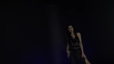 Siyah arka planda yavaşça dans eden at kuyruklu çekici bir kadın. Güzel Asyalı seksi kız kameraya bakıyor, flört ediyor, kırmızı ve mavi ışık, şehir tarzı.