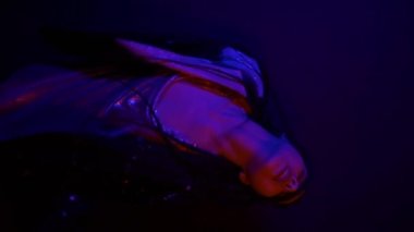 Çok renkli, mavi ışık saçan, kameraya bakan havalı Asyalı genç bir kadının dikey videosu. Şehir tarzı. Neon Moda Hipster eğilimi