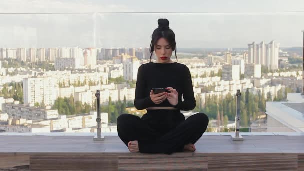 美しい女性は横足に座り 瞑想を実践しています 内なる調和とバランス 屋上テラスでヨガで黒い服の女性 自己認識を実践する — ストック動画
