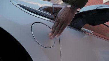 Afrikalı erkek eller EV vagonuna güç bağlantısı yerleştiriyor, yakın plan. Tanımlanamayan Afrikalı adam elektrikli araca kablo bağlıyor ve pilleri şarj ediyor.
