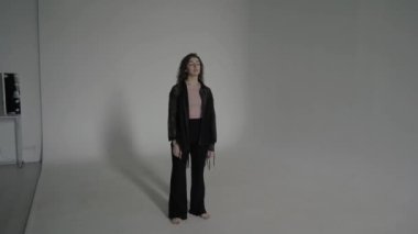 Modaya uygun, siyah elbiseli seksi kıvırcık kadın. Gözleri kapalı, çıplak ayakla fotoğraf stüdyosunda.