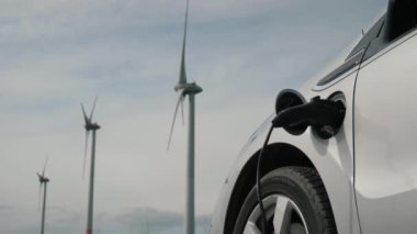 EV araba temiz enerji konsepti. Rüzgar şarj istasyonundan gelen elektrik EV bataryasını doğrudan sürdürülebilir elektrik jeneratörü, ilerleyen yel değirmeni, yakınlardaki rüzgar türbini çiftliğinden şarj ediyor.