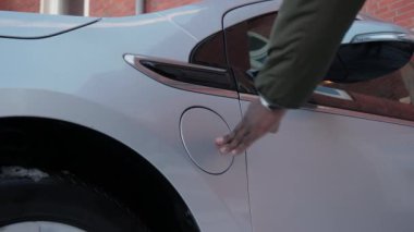 Tanınmayan Afrikalı adam elektrikli araca kablo bağlıyor ve bataryaları şarj ediyor, yakın plan. Afrikalı erkek eller EV vagonuna güç bağlantısı kuruyor