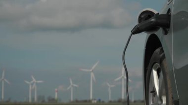 EV araba temiz enerji konsepti, kopyalama alanı. Rüzgar istasyonundan gelen elektrik, EV bataryasını doğrudan sürdürülebilir elektrik jeneratörü, ilerleyen rüzgar değirmeni, otoyol yakınındaki rüzgar türbini çiftliği ile şarj ediyor.