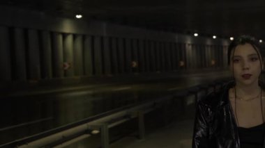 Köprü fotokopi alanının altında siyah ceketli bir kadın duruyor. Asyalı bir kadın arabalı bir yolun arka planında kameraya bakıyor.