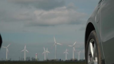 Erkek el, EV vagonuna, rüzgar şarj istasyonuna, otoyola yakın bir rüzgar türbini çiftliğine güç bağlayıcı yerleştiriyor. Tanımlanamayan adam elektrik kablosunu elektrikli araca, sürdürülebilir elektriğe, yel değirmenine bağlıyor