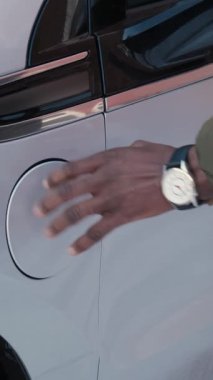 Afrikalı erkeklerin güç bağlantısını EV 'ye bağladıkları dikey video, yakın plan. Tanınmayan Afrikalı adam elektrikli araca kablo yerleştiriyor ve pilleri şarj ediyor