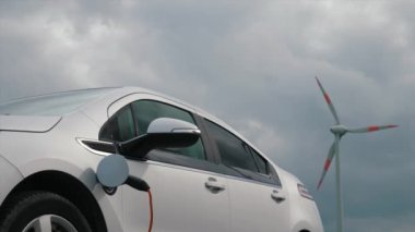 Yenilenebilir enerji kullanan elektrikli araç. Yel değirmenlerinin arka planında şarj olan EV ya da PHEV arabası, kopyalama alanı. Elektrikli araba aküsünü şarj et. Yel değirmeni, rüzgar türbini çiftliği.