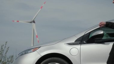 Adam elektrik kablosunu sürdürülebilir elektrik jeneratörü, yel değirmeni, rüzgar türbini yakınındaki elektrikli araca bağlıyor. Erkek el güç bağlantısını EV vagonuna yerleştirir, rüzgar şarj istasyonu