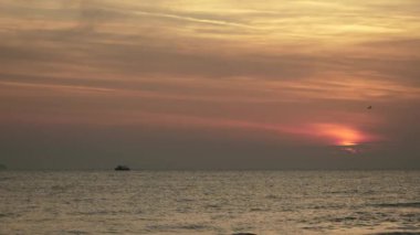 Gün batımının nefes kesici görüntüsü sakin okyanus sularını güzel bir şekilde yansıtıyor balıkçı gemisiyle, yumuşak turuncu ve pembe renkli gökyüzünü, inanılmaz derecede huzurlu bir atmosfer yaratıyor.