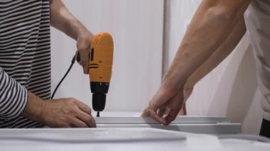 Deneyimli erkek eller mobilyaları elektrikli matkapla birleştiriyor ve DIY projelerinde etkili takım çalışması sergiliyor. Başarılı sonuçlar için gerekli olan kalite işçiliği ve yaratıcılığa güçlü bir adanmışlık