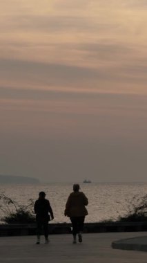 Tanımlanamayan insanların deniz kenarında yürüyüp uzayı kopyaladığı dikey bir video. Şafak vakti deniz kenarındaki toprak yol.