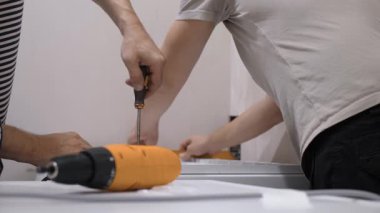 Tanımlanamayan iki kişi mobilyaları, takım çalışmasını ve becerilerini bir araya getirmek için birlikte çalışıyorlar. Tornavida, onarımın verimliliğini vurgulayarak DIY yaklaşımını yansıtır.