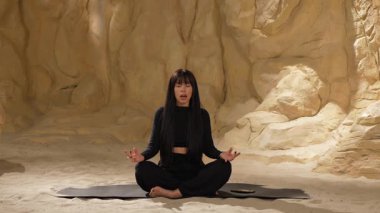 Çöl kumulu meditasyonu. Siyah elbiseli güzel bir kadın, kapalı gözlerle karemat üzerinde oturur, parmaklarını sayar, iç uyum dengesini hisseder, özfarkındalığı geliştirir, stresten arınır.