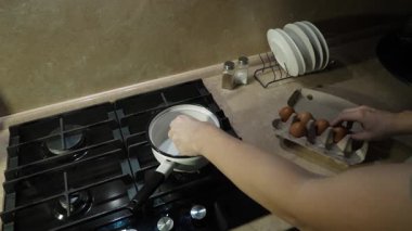 Sıcak mutfakta, insan arka planda düzgün yerleştirilmiş tabaklarla taze yumurta kaynatmaya hazırlanır. Bu an kahvaltı hazırlığının hazzını yakalıyor.