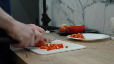 Modern bir mutfakta kesme tahtasında taze kırmızı biber doğrayan eller. Bu, aşçılık tekniklerini ve günlük rutinlerde kullanılan modern yemek aletlerini ön plana çıkarır.