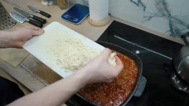 Erkek eller yemeğe peynir ekler, mükemmel ev yapımı yemekler ve lezzetli bir mutfak deneyimi için kesme ve katmanlama tekniklerini vurgular.