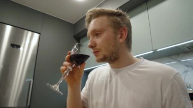 Düşünceli ve düşünceli bir birey şık, modern dekorasyon ve mobilyaların ortasındaki bir rahatlama ve zevk anını gösteren modern bir mutfakta cömert bir kadeh kırmızı şarabın tadını çıkarıyor.