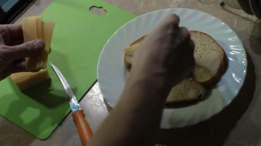 Eller taze pişmiş ekmeğin üzerine peynir dilimleri koyar. Bu enfes mutfak sahnesi evde gurme aperatifleri hazırlamanın özünü yansıtıyor.