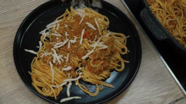 Elleri, siyah tabakta lezzetli spagettiye rendelenmiş peynir ekliyor. Şeflerin yeteneğini ve otantik İtalyan mutfağının canlı, aromatik aromasını vurguluyor.