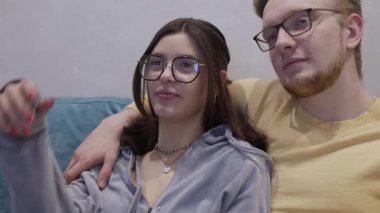 Gözlüklü genç çift, evlerinde kanepede rahat bir film gecesinin tadını çıkarıyorlar. Birbirlerine olan derin sevgilerini ve güçlü bağlarını vurguluyorlar. Sıcak atmosfer birbirlerinden hoşlandıklarını gösteriyor.