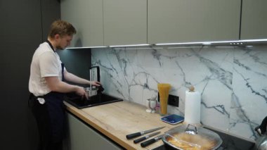 Deneyimli aşçı bir tencereyi musluk suyuyla doldurur ve tam teçhizatlı bir mutfakta yemek hazırlamaya başlar. Bu da hassas ve gelişmiş teknikleri kaliteli aletlerle gösterir.