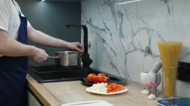 Yetenekli bir şef tencereyi musluk suyuyla doldurur, renkli sebzeler pişirir ve modern bir tezgahta makarna pişirir.