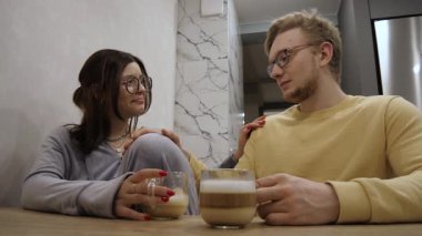 Bardaklı sevimli çift, bir fincan kahve içerken, sıcak bir gülümseme ve romantik temalar için ideal, güzel dekore edilmiş bir yerde samimi anlar paylaşmaktan zevk alır.